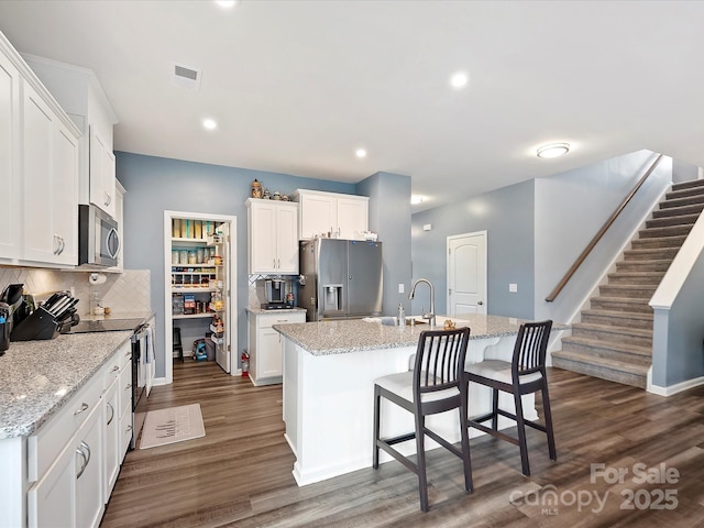 kitchen featuring stainless steel appliances, tasteful backsplash, dark wood-style flooring, and a kitchen island with sink