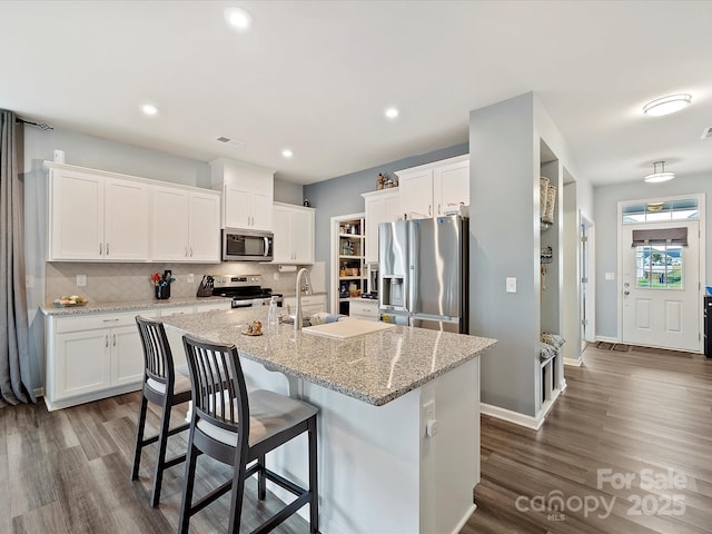 kitchen featuring tasteful backsplash, white cabinets, an island with sink, dark wood-style floors, and stainless steel appliances