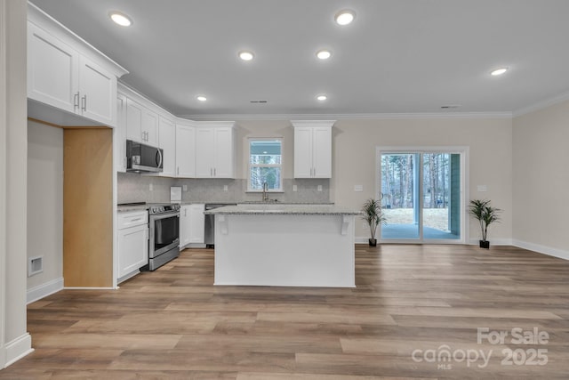 kitchen with stainless steel range with electric stovetop, white cabinets, crown molding, and a center island