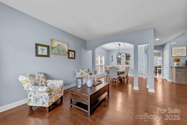 living room featuring arched walkways, baseboards, and wood finished floors