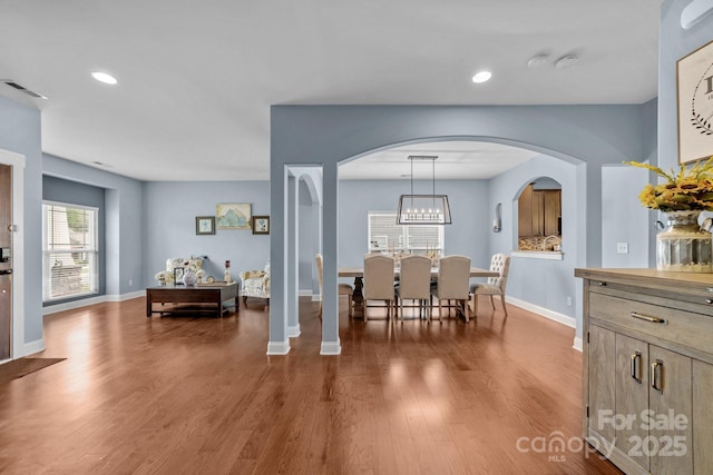 dining room with arched walkways, wood finished floors, visible vents, and baseboards