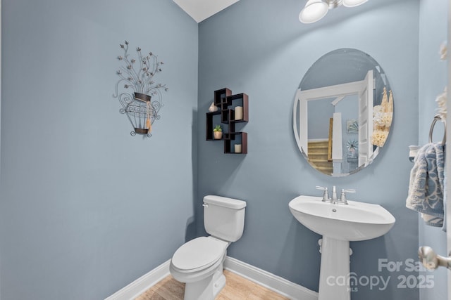 half bath featuring toilet, a sink, baseboards, and wood finished floors