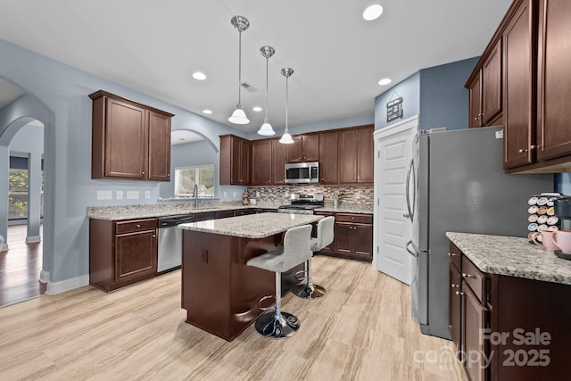 kitchen featuring arched walkways, a kitchen island, appliances with stainless steel finishes, light wood finished floors, and a kitchen bar