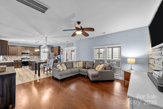 living area featuring ceiling fan with notable chandelier, wood finished floors, and visible vents