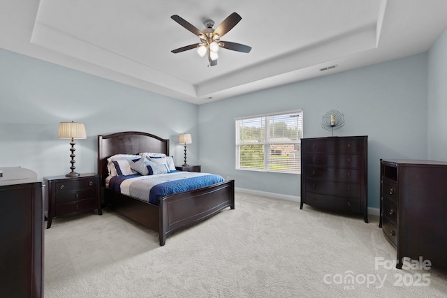 bedroom with a tray ceiling, light colored carpet, visible vents, and baseboards