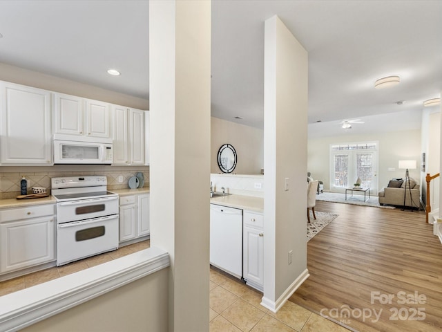 kitchen featuring decorative backsplash, white appliances, white cabinets, and light countertops