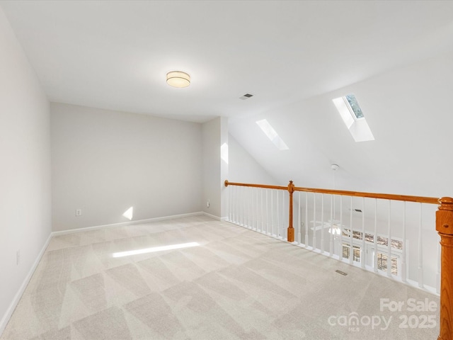 carpeted empty room with lofted ceiling with skylight, baseboards, and visible vents