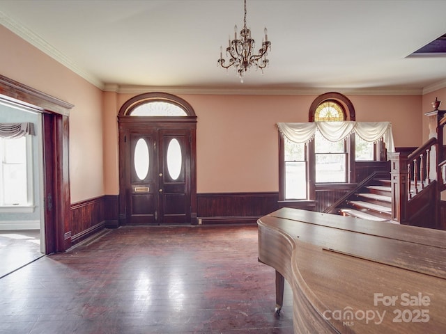 foyer entrance with an inviting chandelier, stairway, a wealth of natural light, and wainscoting