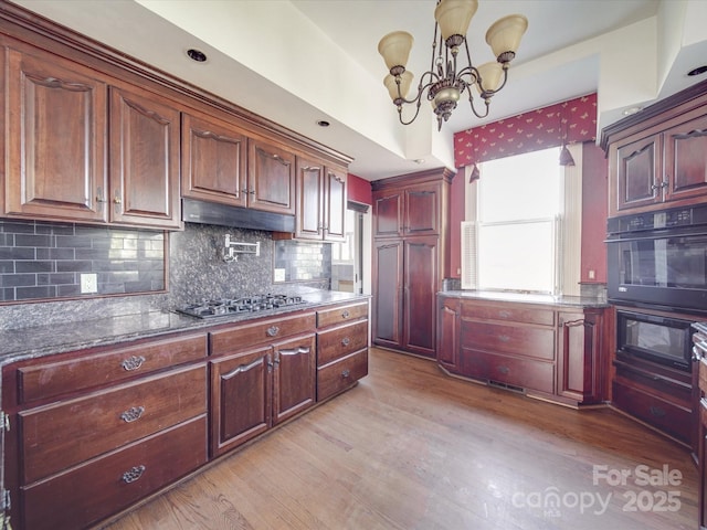 kitchen with light wood-style flooring, a notable chandelier, under cabinet range hood, oven, and stainless steel gas stovetop