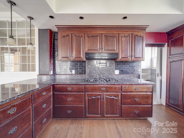 kitchen with tasteful backsplash, light wood-style floors, dark brown cabinets, under cabinet range hood, and stainless steel gas stovetop