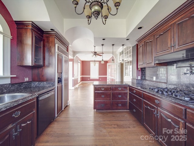 kitchen with arched walkways, black gas cooktop, stainless steel dishwasher, wood finished floors, and a peninsula