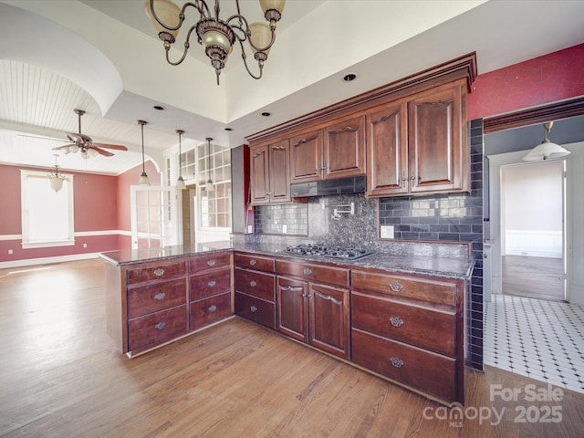 kitchen with stainless steel gas cooktop, backsplash, light wood-style floors, a peninsula, and under cabinet range hood