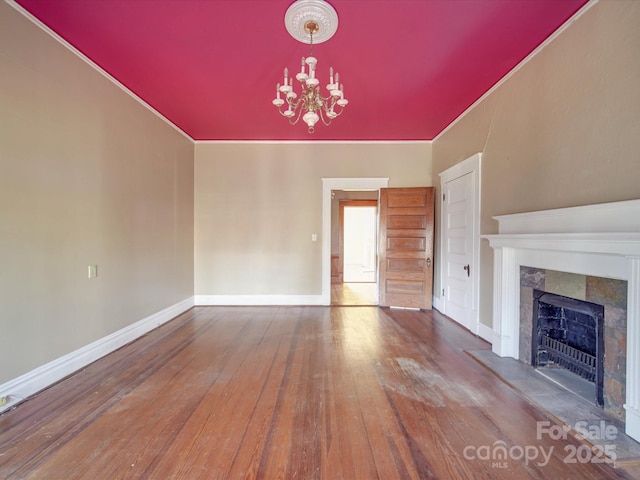 unfurnished living room featuring hardwood / wood-style floors, a premium fireplace, baseboards, and a notable chandelier