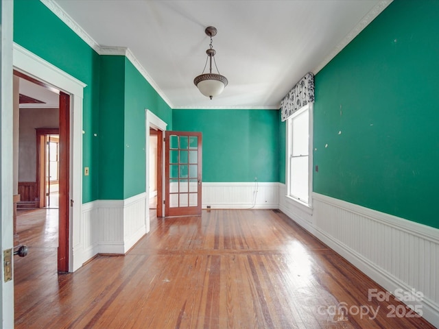 spare room with a wainscoted wall, wood finished floors, and crown molding