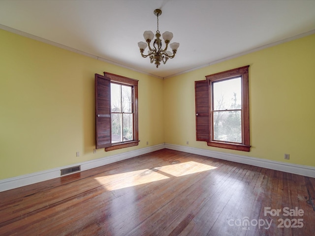 spare room featuring visible vents, a chandelier, hardwood / wood-style floors, and ornamental molding