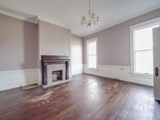 unfurnished living room with wainscoting, a premium fireplace, ornamental molding, hardwood / wood-style floors, and an inviting chandelier