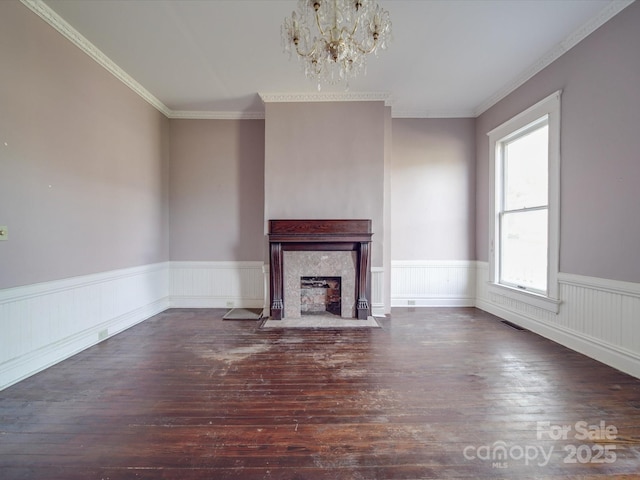 unfurnished living room with visible vents, a wainscoted wall, wood finished floors, an inviting chandelier, and a fireplace