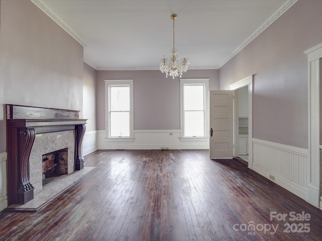 unfurnished living room featuring dark wood-type flooring, wainscoting, a high end fireplace, and an inviting chandelier