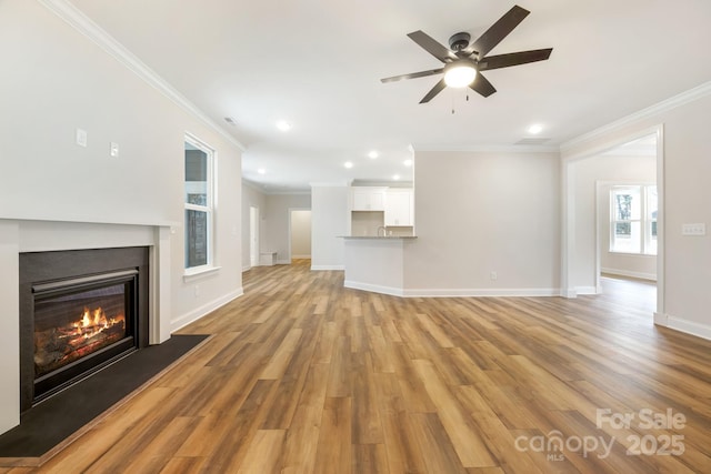 unfurnished living room featuring light wood-type flooring, baseboards, ornamental molding, and a glass covered fireplace