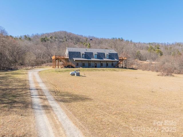 view of front of house with driveway, a forest view, stairway, and a front yard