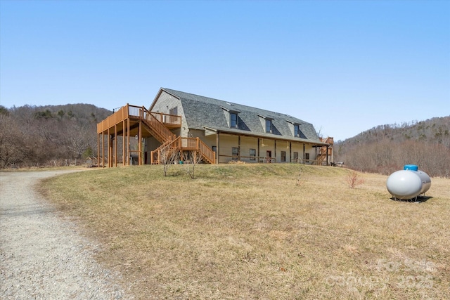 exterior space with a shingled roof, a gambrel roof, stairway, a wooden deck, and a front yard