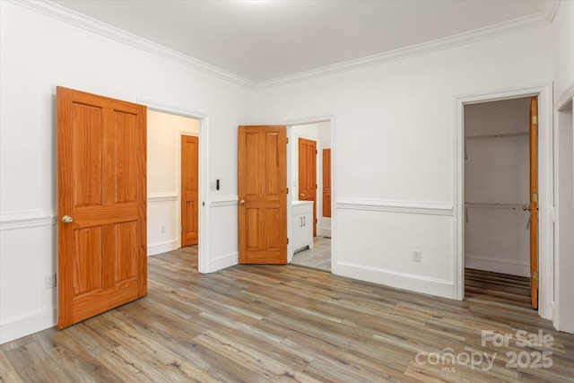 unfurnished bedroom with light wood finished floors, a spacious closet, ornamental molding, and a closet