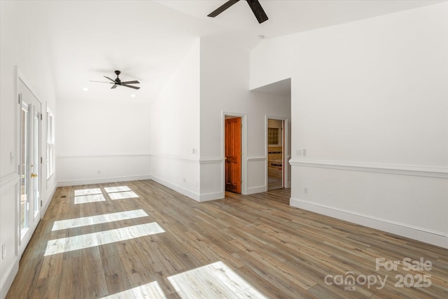 spare room with baseboards, ceiling fan, high vaulted ceiling, and wood finished floors