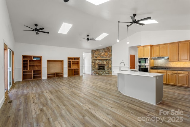 kitchen with a skylight, light wood-style flooring, open floor plan, stainless steel double oven, and a stone fireplace