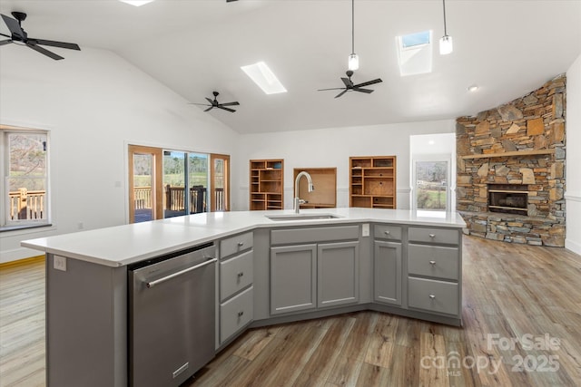 kitchen with gray cabinets, stainless steel dishwasher, open floor plan, a sink, and vaulted ceiling with skylight