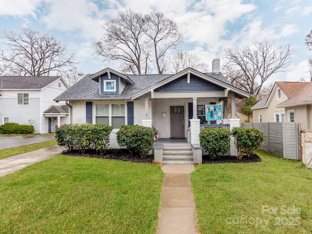 bungalow featuring fence, a porch, a shingled roof, a front lawn, and brick siding