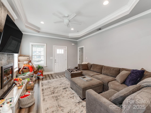 living room featuring wood finished floors, crown molding, a tray ceiling, and a premium fireplace