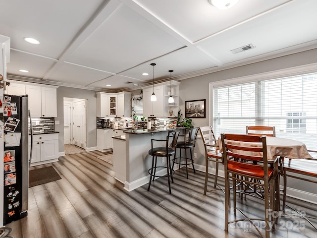 kitchen with a breakfast bar area, visible vents, freestanding refrigerator, dark countertops, and backsplash