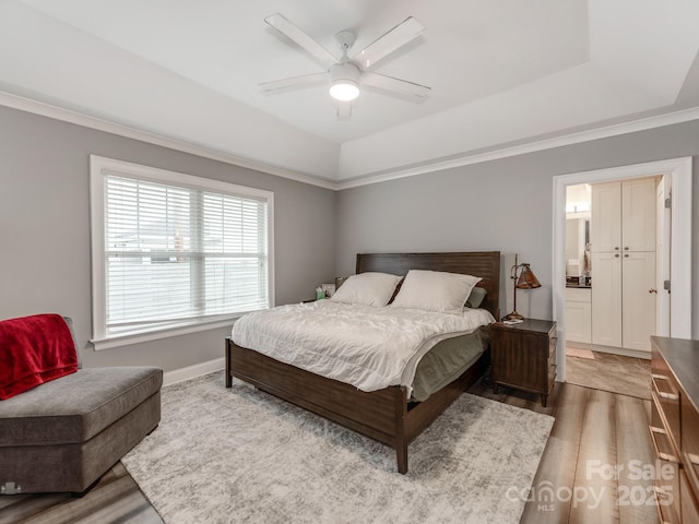 bedroom featuring ensuite bathroom, light wood-type flooring, a raised ceiling, and a ceiling fan