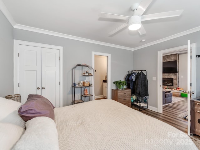 bedroom with wood finished floors, a closet, a fireplace, crown molding, and ceiling fan