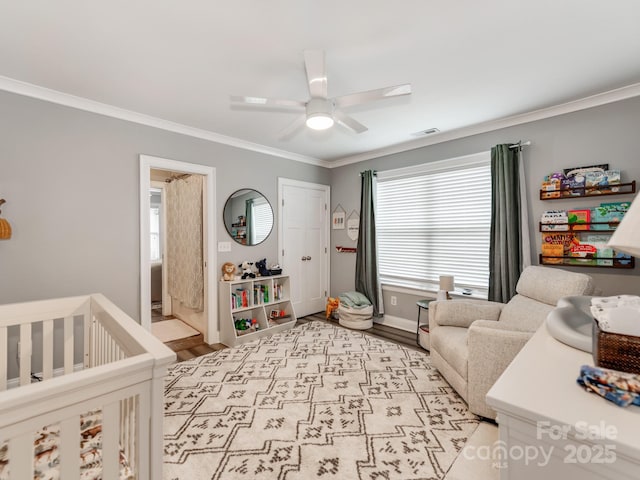 bedroom featuring a ceiling fan, visible vents, a nursery area, light wood-style floors, and crown molding