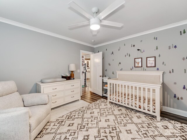 bedroom with baseboards, crown molding, a nursery area, and a ceiling fan