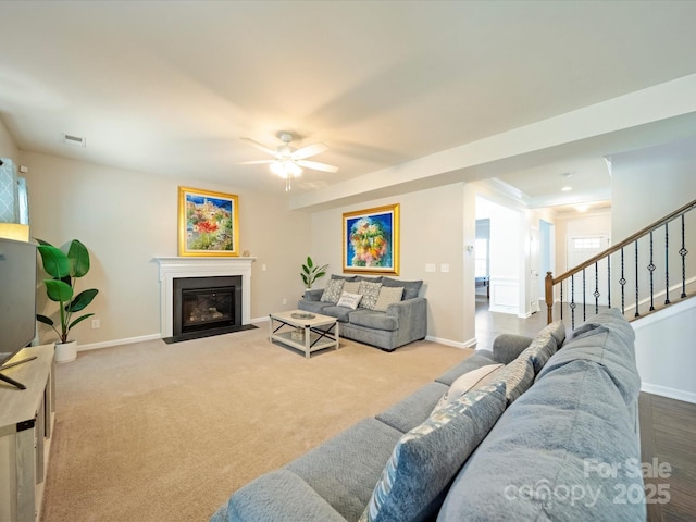 carpeted living area with a fireplace with flush hearth, visible vents, stairway, and baseboards