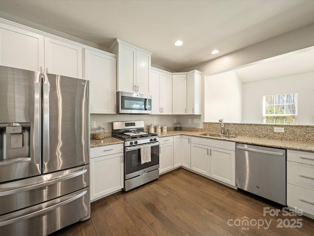 kitchen featuring a sink, white cabinetry, appliances with stainless steel finishes, light stone countertops, and dark wood finished floors