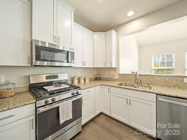 kitchen featuring light stone counters, stainless steel appliances, a sink, white cabinetry, and dark wood-style floors