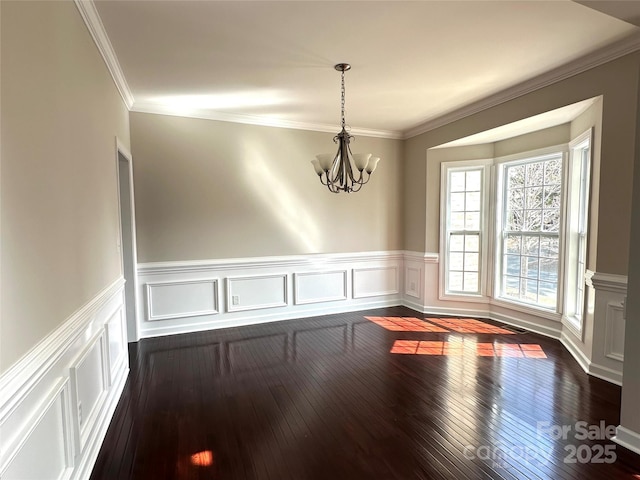 unfurnished dining area with a chandelier, a wainscoted wall, dark wood-style floors, and crown molding