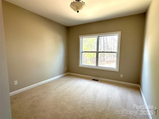 spare room featuring light colored carpet, visible vents, and baseboards