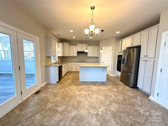 kitchen with under cabinet range hood, visible vents, light stone countertops, black appliances, and tasteful backsplash