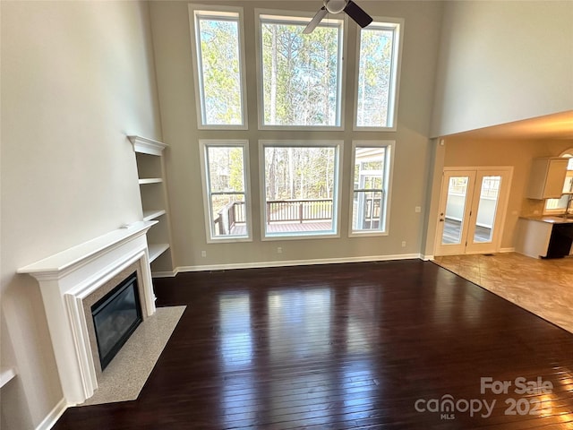 unfurnished living room with a high end fireplace, a high ceiling, baseboards, and hardwood / wood-style flooring