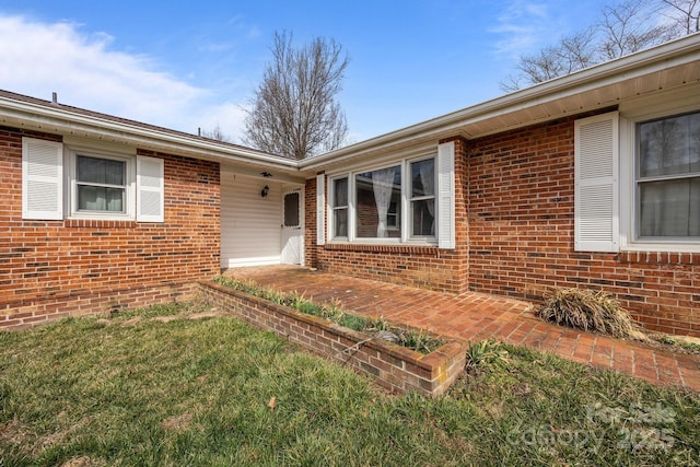 entrance to property featuring brick siding and a lawn