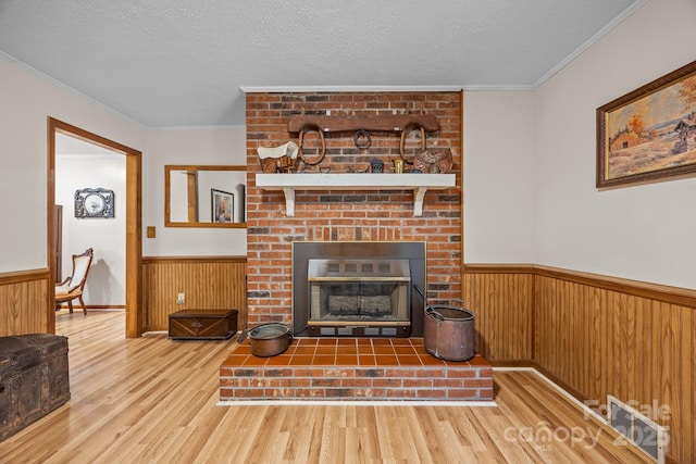 living room featuring ornamental molding, a brick fireplace, wainscoting, and a textured ceiling