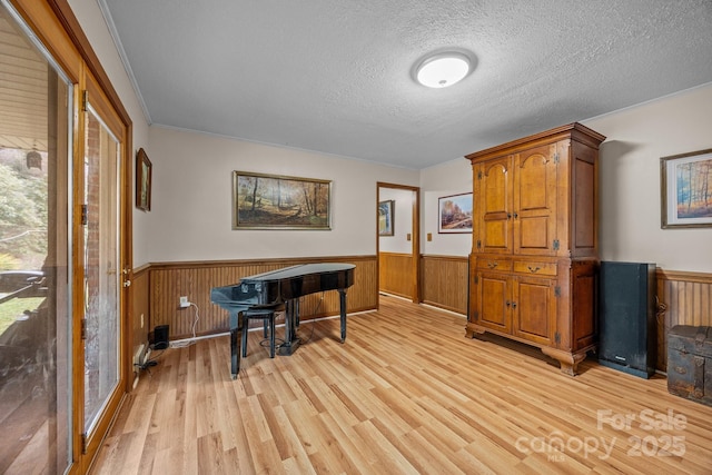 office area featuring light wood-style flooring, a textured ceiling, and wainscoting