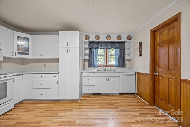 kitchen featuring a wainscoted wall, light countertops, ornamental molding, a sink, and white appliances