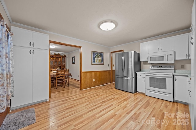 kitchen featuring a wainscoted wall, light wood finished floors, light countertops, white cabinets, and white appliances