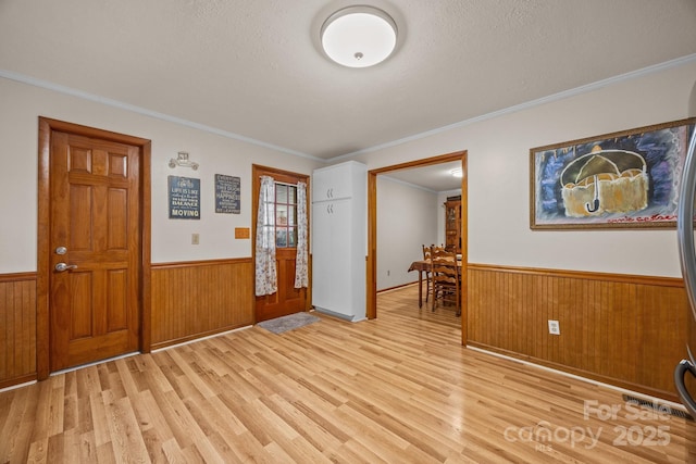 entryway with a wainscoted wall, light wood finished floors, a textured ceiling, and wood walls