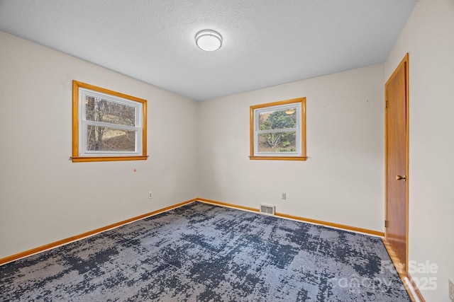 unfurnished room with a textured ceiling, carpet flooring, visible vents, and baseboards